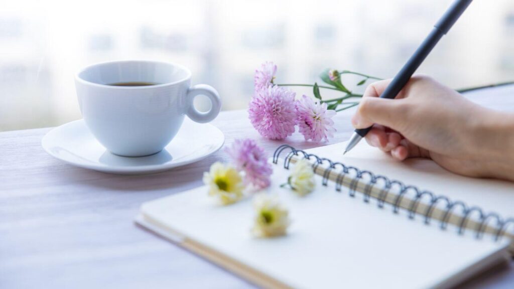 コーヒーと花に囲まれて夢ノートに書き込む手元